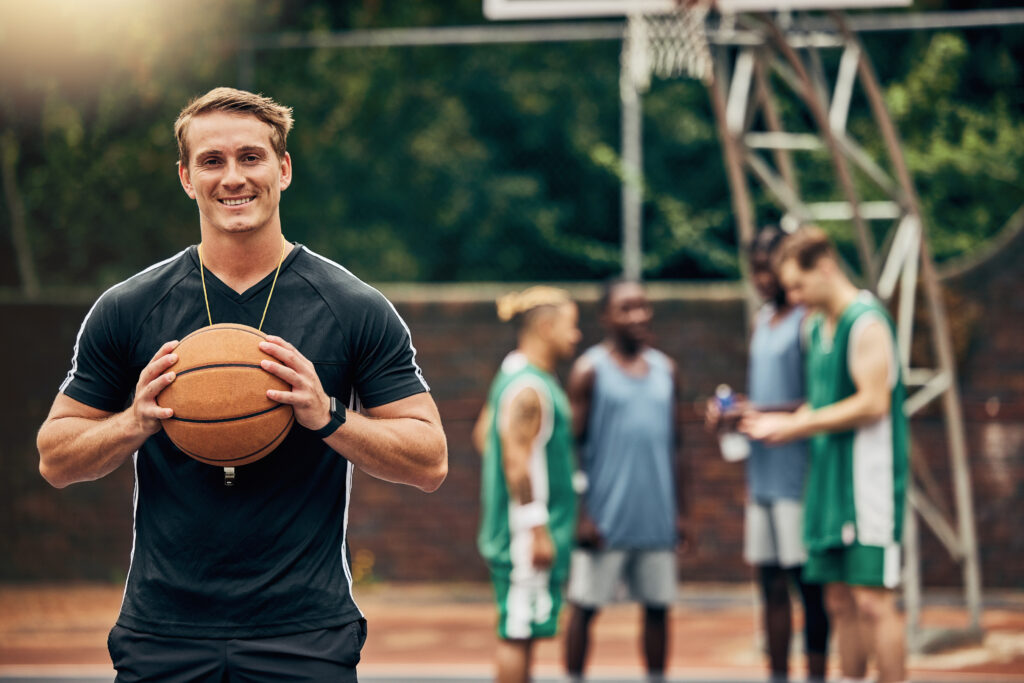 Outdoor basketball court, coach and happy man portrait training, collaboration and sports for college athlete team, professional player and fitness group. Proud, smile and teaching expert game skills.
